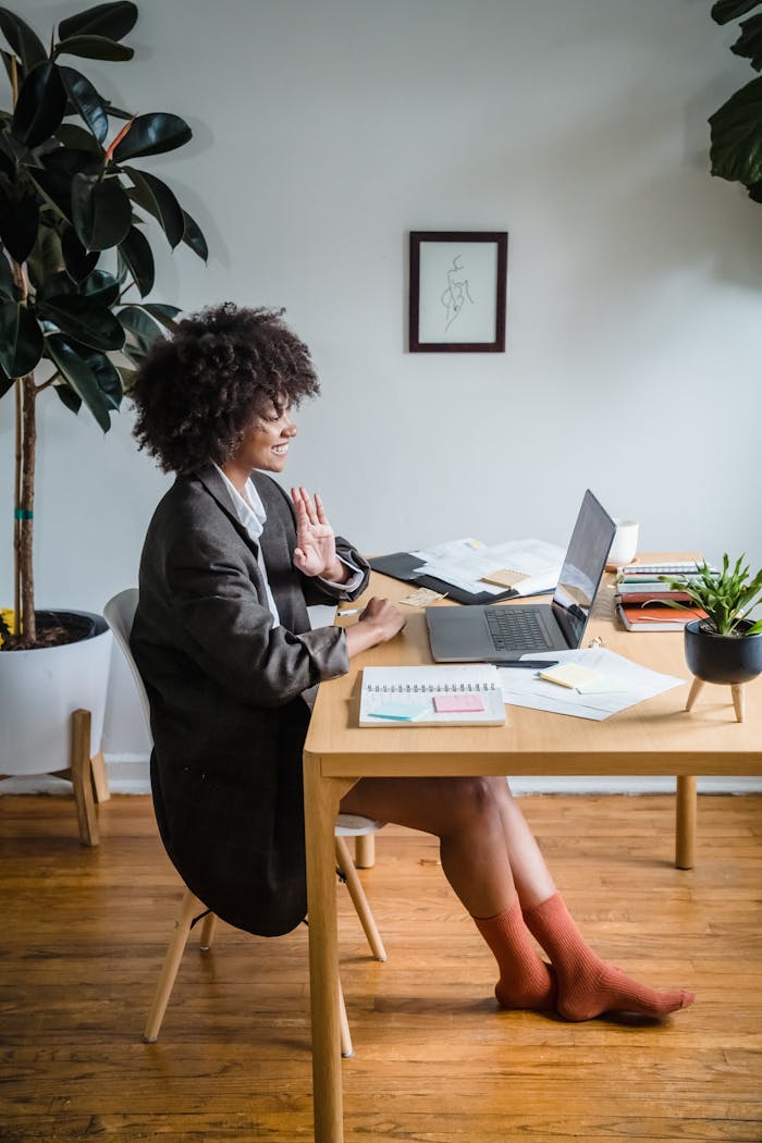 Businesswoman in a suit working remotely, using a laptop for a video call inside a modern home office.