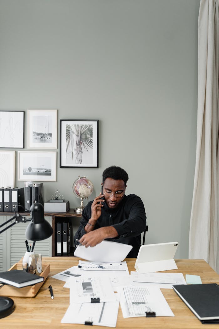 Black accountant managing documents and phone calls in a modern office setting.