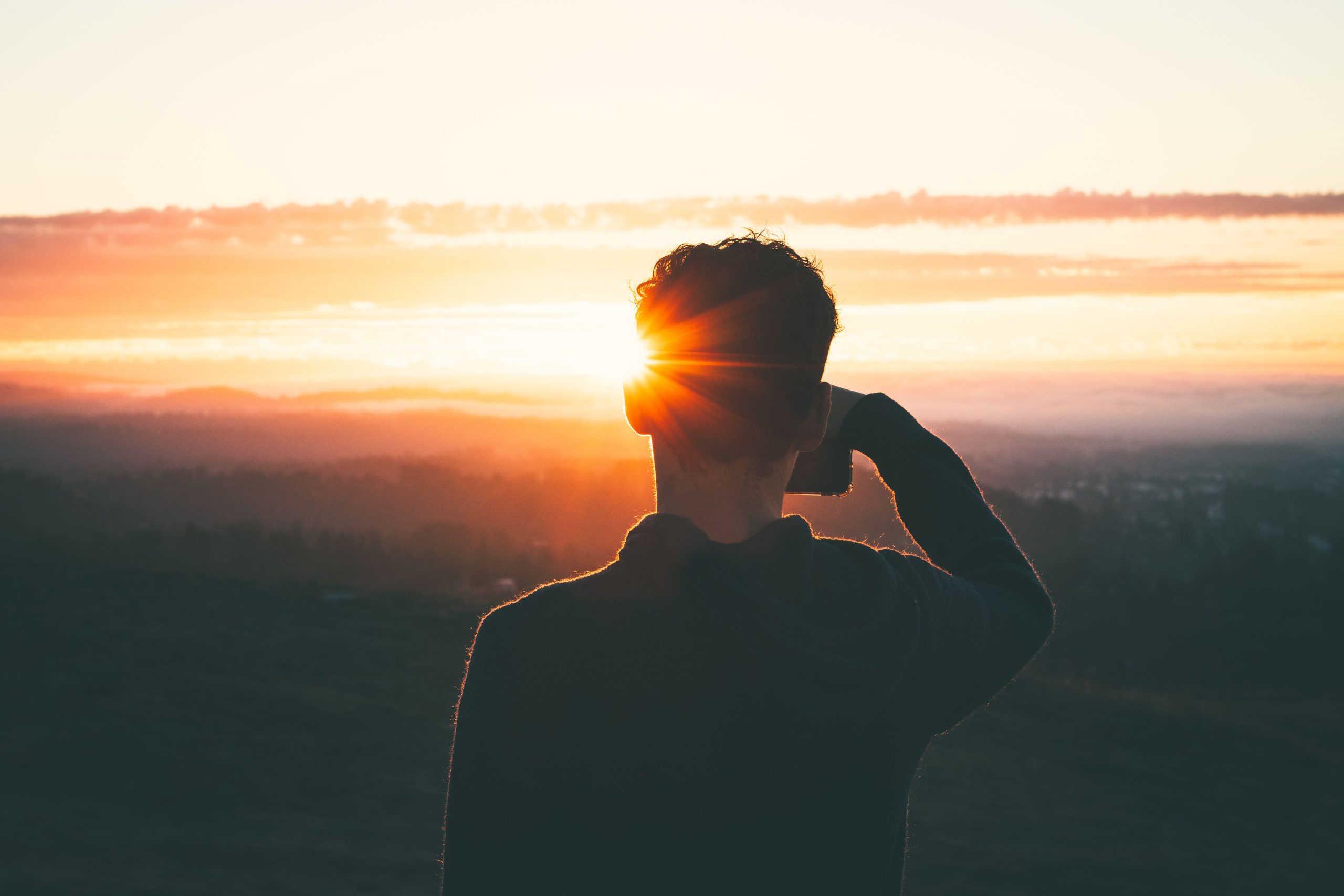 Silhouette of a man at sunrise, capturing the vibrant sky and serene landscape